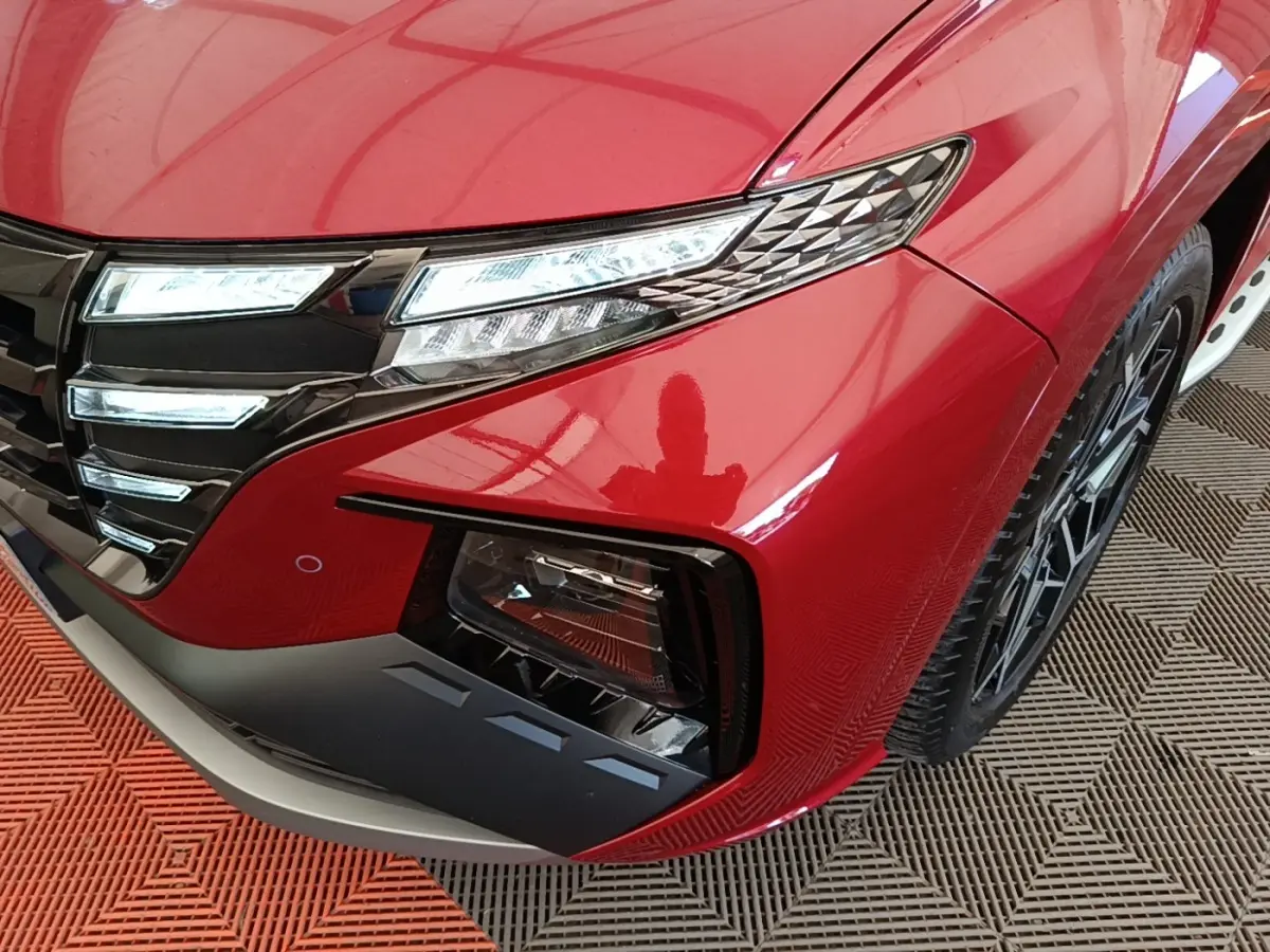 Gros plan sur l'avant droit rouge du Hyundai Tucson 2022, mettant en valeur les phares LED et la calandre noire brillante.