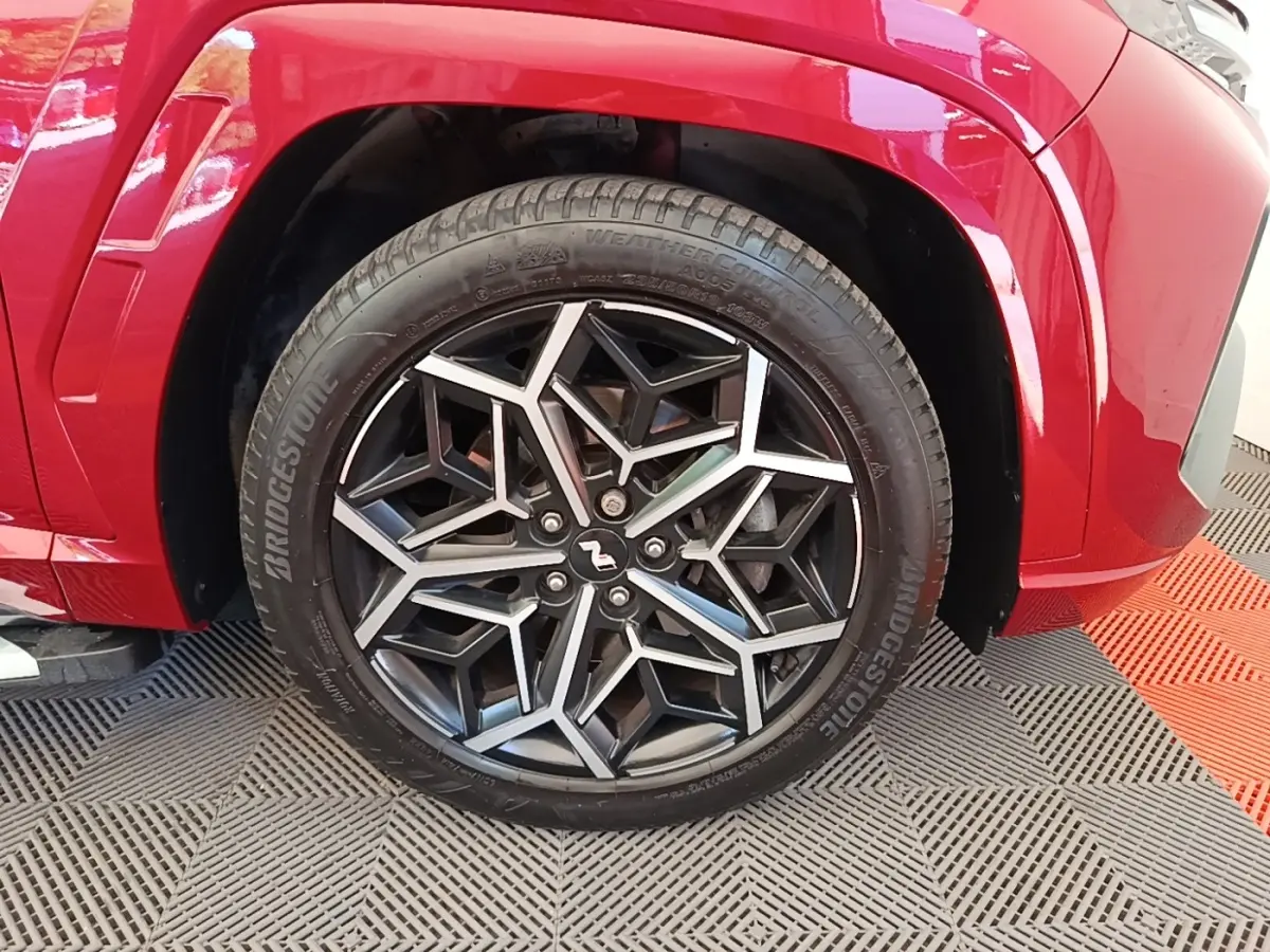 Gros plan sur la roue avant gauche du Hyundai Tucson rouge, avec jante alliage noire et argentée au design géométrique N Line.