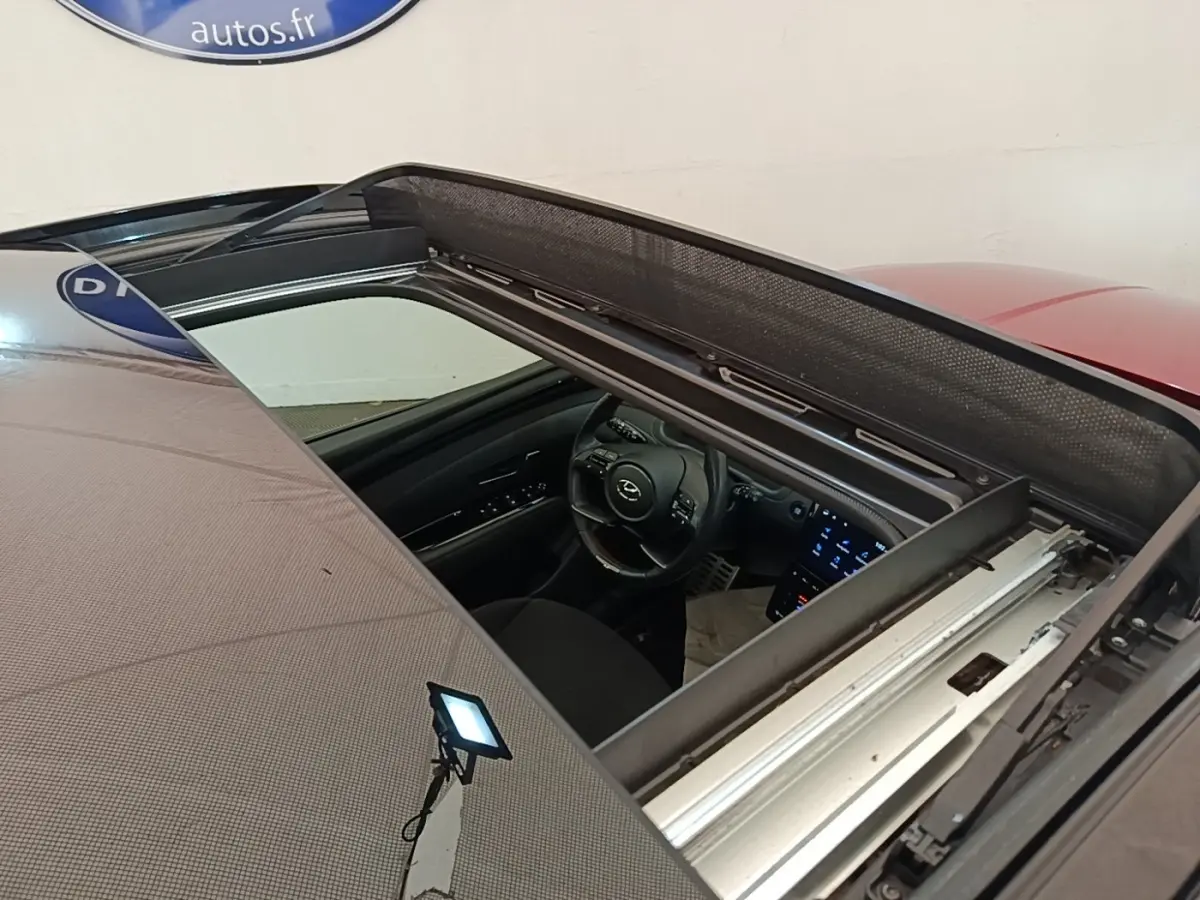 Vue plongeante sur l'intérieur via toit ouvrant du Hyundai Tucson rouge, montrant volant et écran tactile allumé.