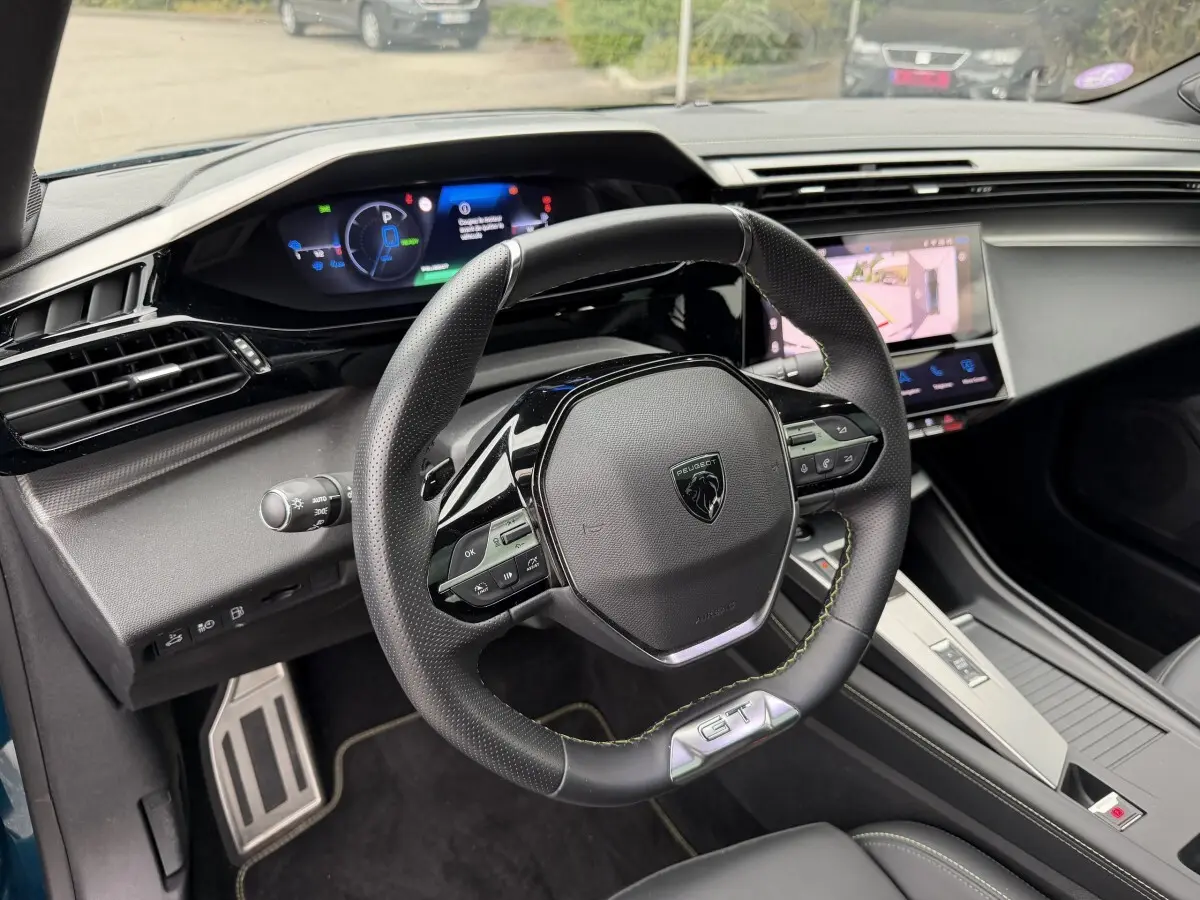 Vue intérieure du poste de conduite de la Peugeot 408 PHEV 225 GT bleu, avec volant multifonction et écran tactile central.