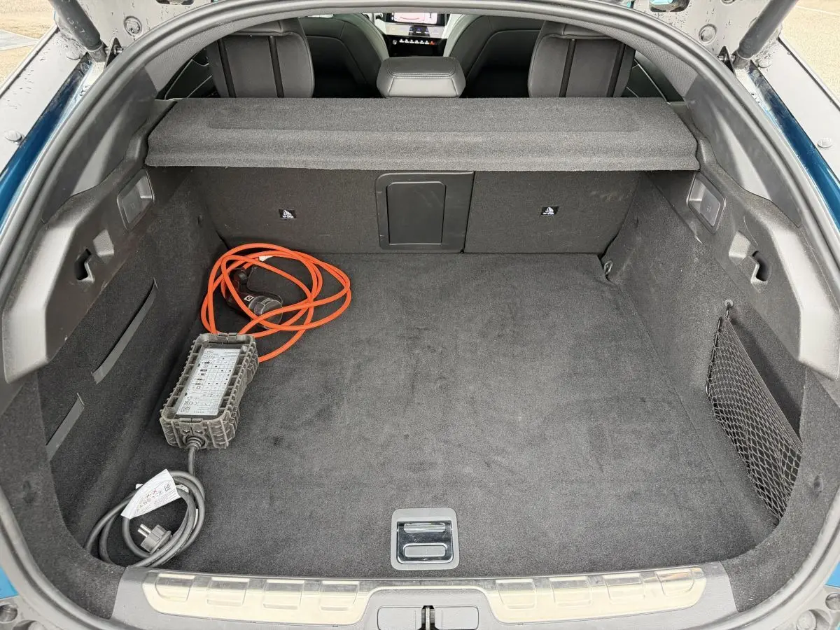 Coffre ouvert d’une Peugeot 408 PHEV 225 GT bleu 2023, montrant la moquette noire et le câble de recharge orange.