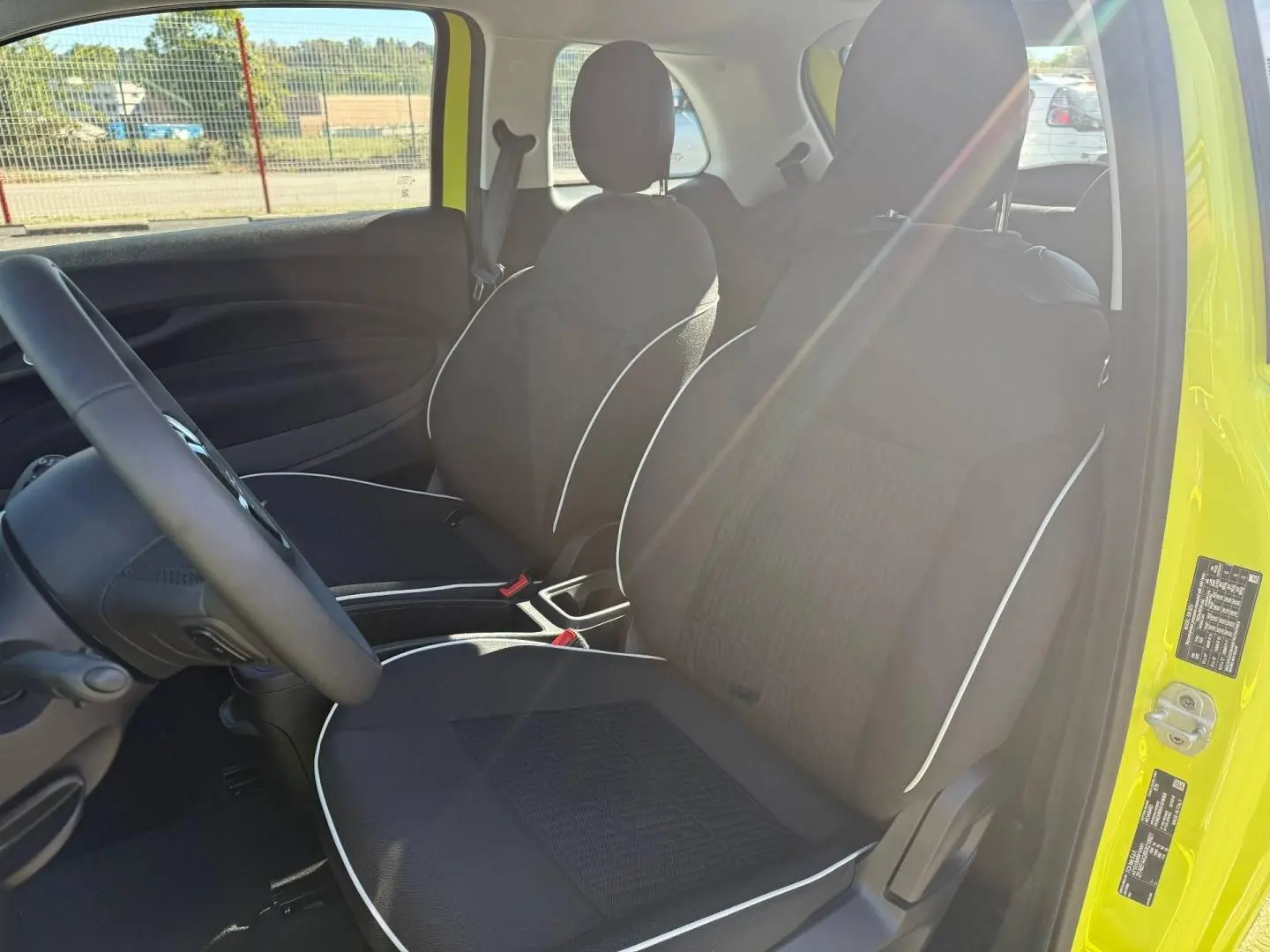Vue intérieure côté conducteur de la Fiat 500 e 95ch MY24 jaune, sièges noirs avec surpiqûres blanches et volant multifonction.