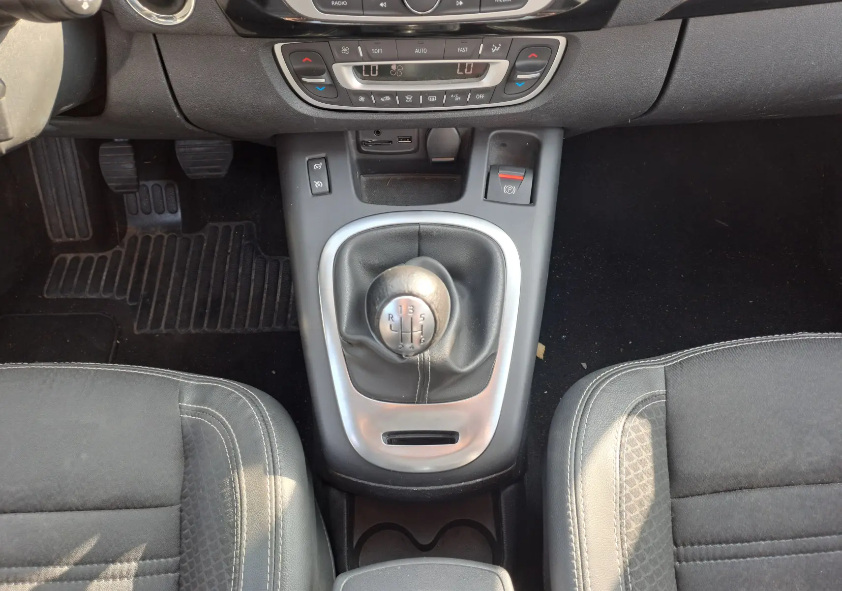 Vue plongeante sur la console centrale du Renault Scenic III gris, mettant en valeur le levier de vitesse manuel et les sièges noirs.