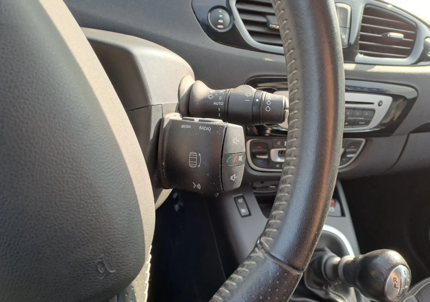 Gros plan sur la commande multimédia et le volant en cuir noir du Renault Scénic III gris, intérieur avant.