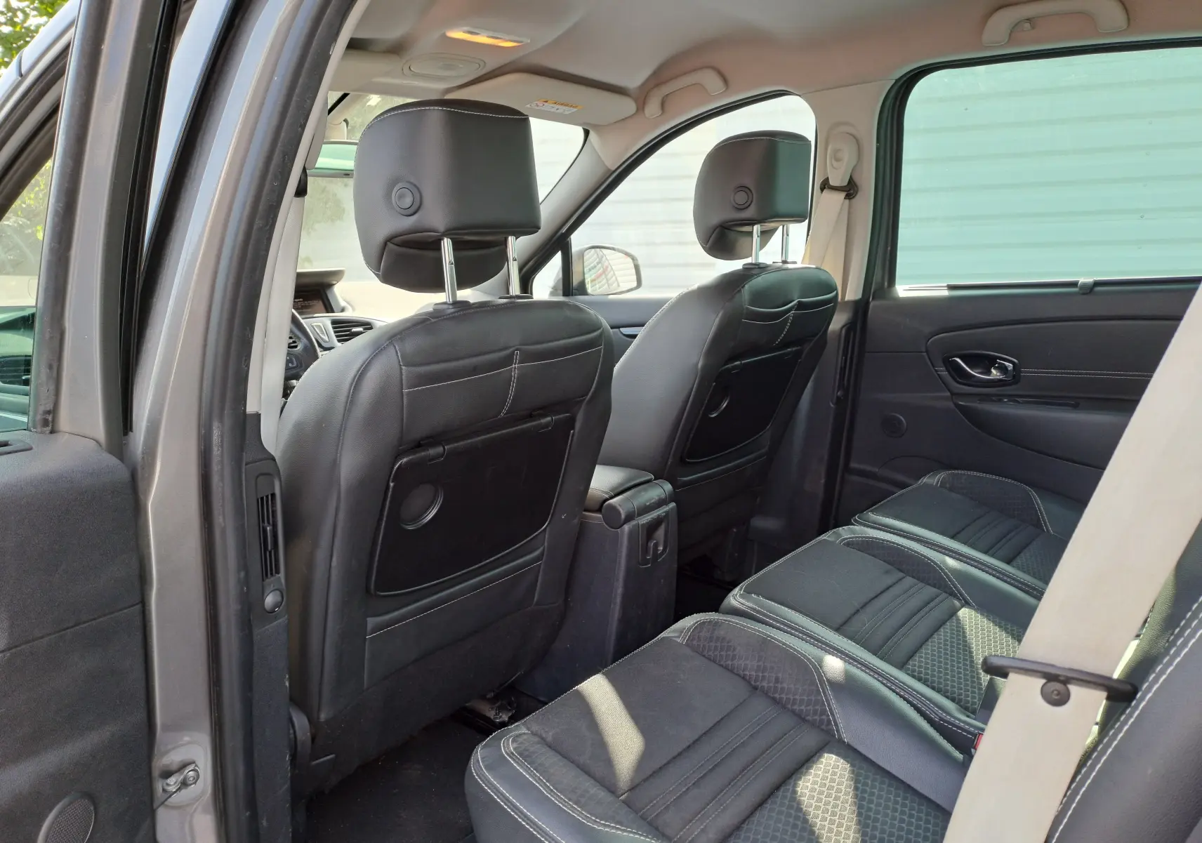 Vue intérieure arrière du Renault Scénic III gris, montrant les sièges en cuir noir et tissu avec ceinture de sécurité beige.