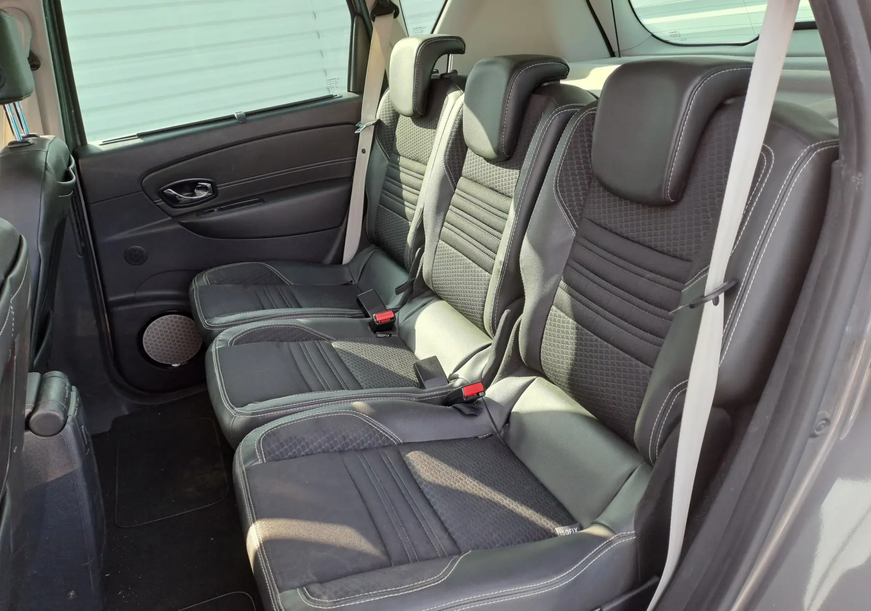 Vue latérale droite des sièges arrière noirs en tissu et cuir du Renault Scenic III gris, montrant trois appuie-têtes et ceintures.