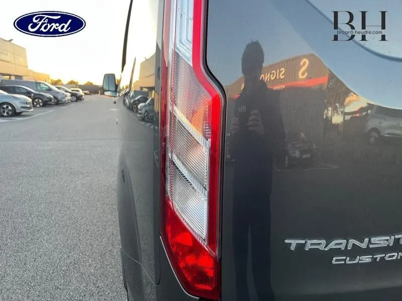 Gros plan sur le feu arrière droit d'un Ford Transit Custom gris Magnétic métallisé, reflet du photographe visible.