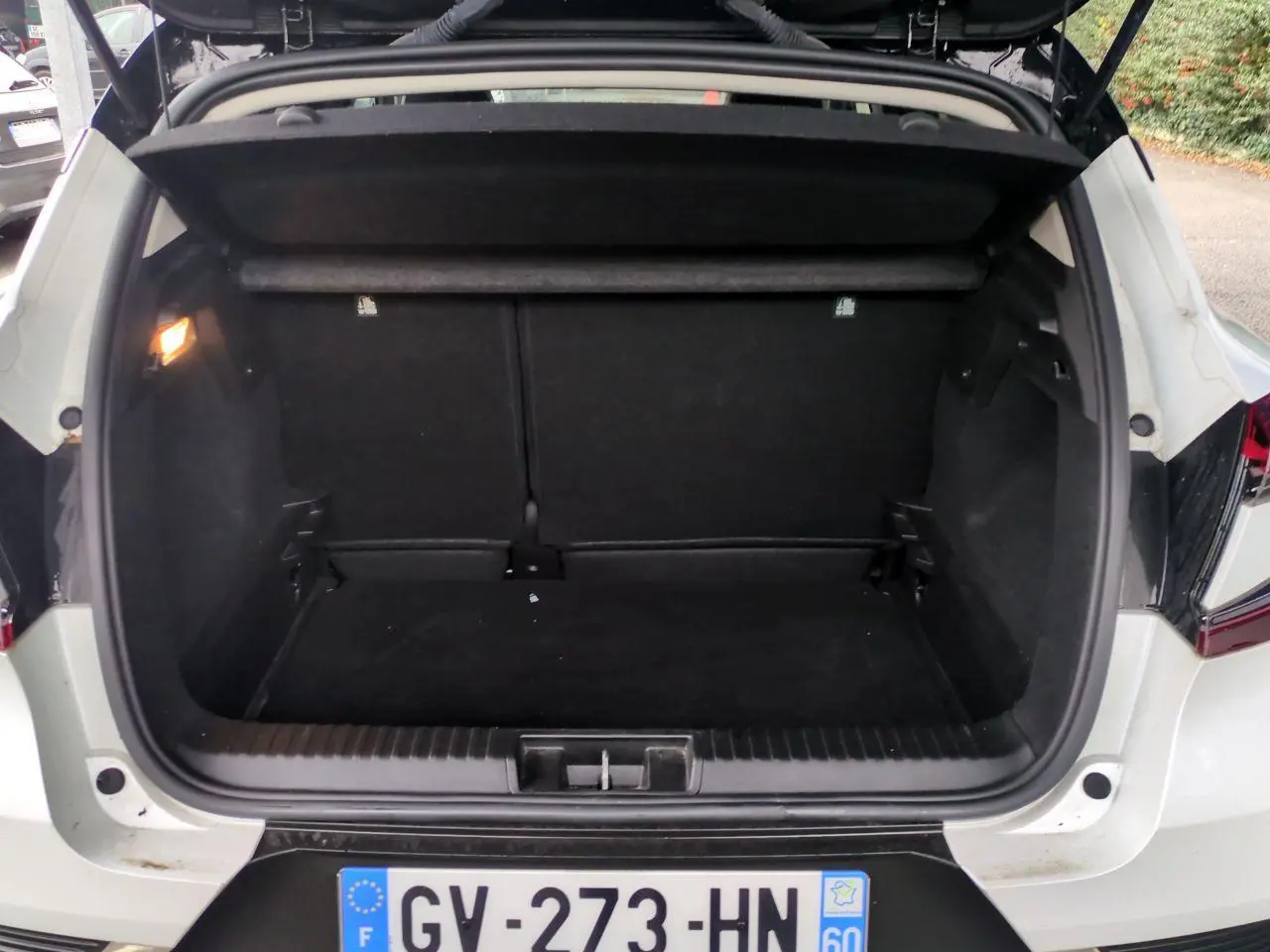 Coffre ouvert vu de l'arrière d'un Renault Captur blanc 2024, avec intérieur de coffre noir et éclairage latéral.
