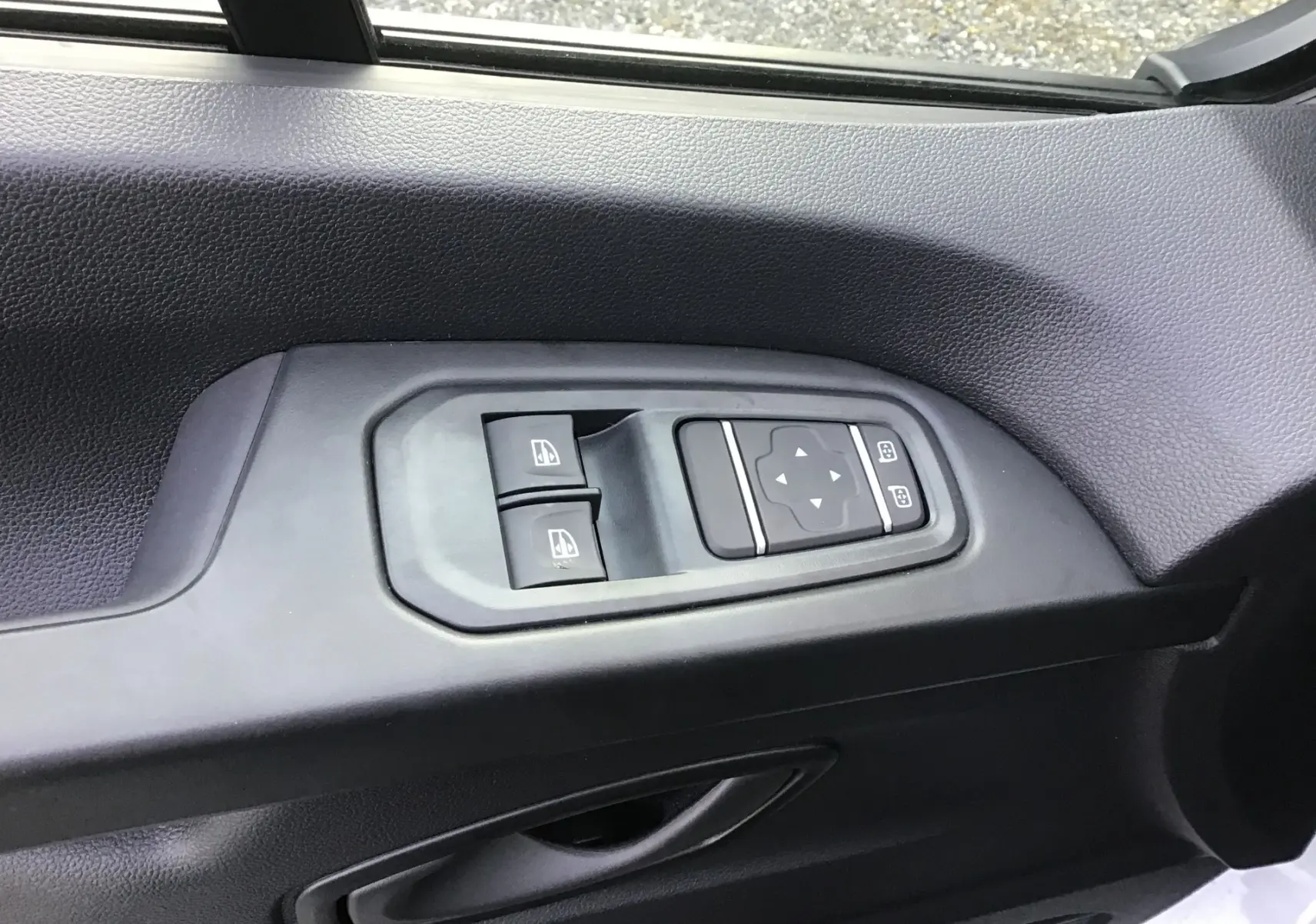 Gros plan sur les commandes de lève-vitres et réglage des rétroviseurs côté gauche du Renault Trafic Fourgon blanc 2025.