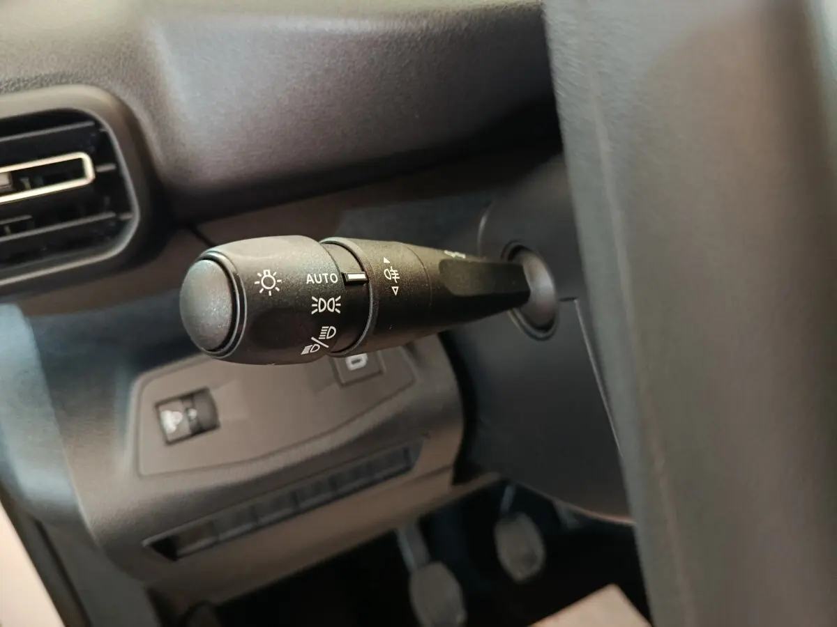 Gros plan sur le commodo des phares à gauche du volant dans l’habitacle sombre du Peugeot Partner blanc 2025.