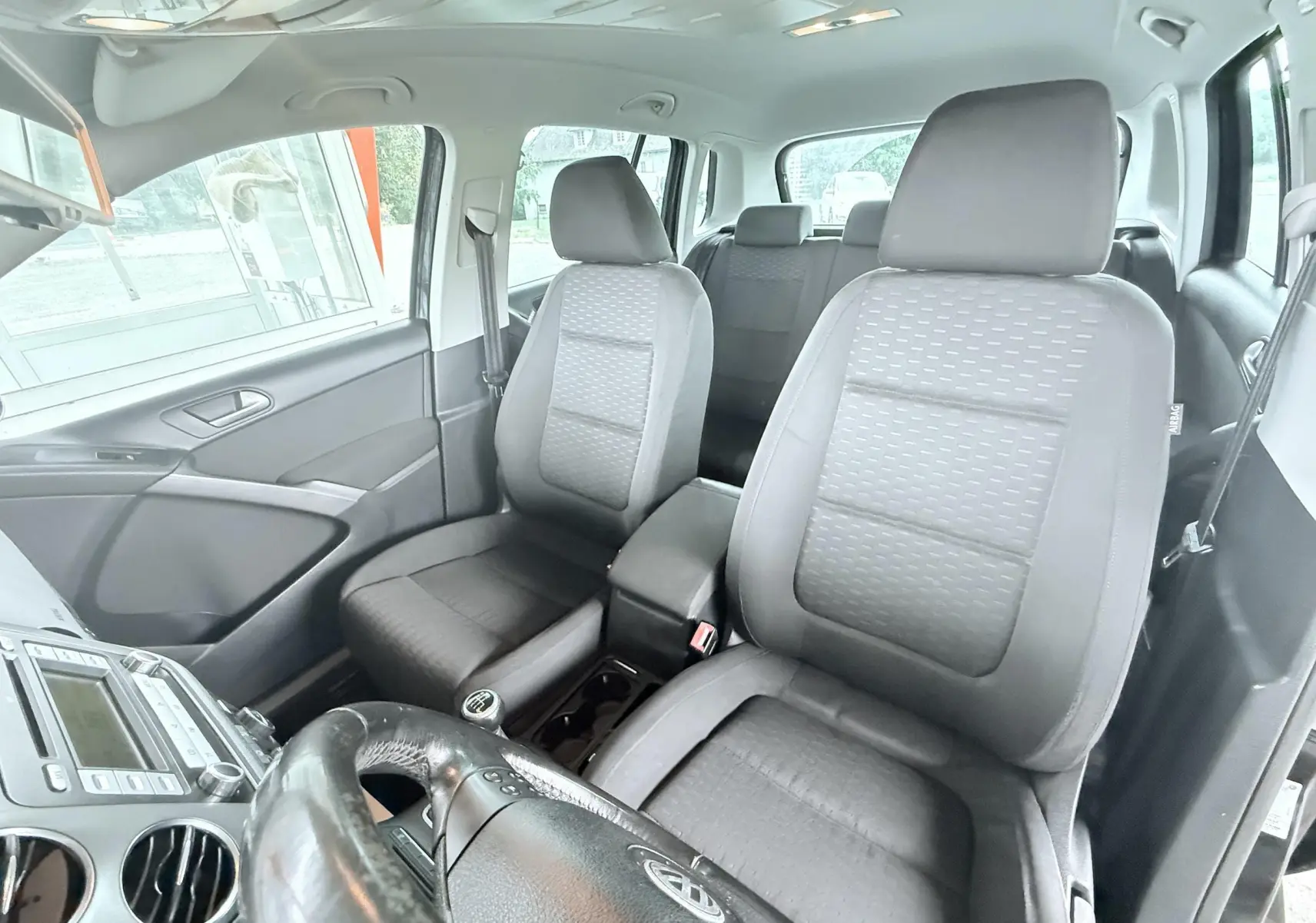 Vue intérieure avant du Volkswagen Tiguan noir 2007, sièges tissu gris et volant multifonctions visible.