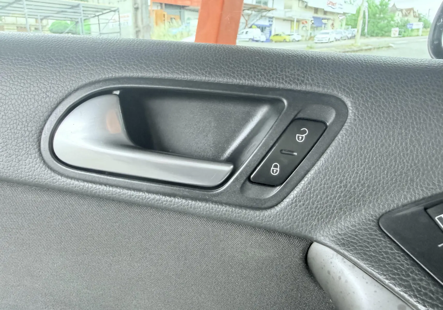 Poignée intérieure de porte côté gauche du Volkswagen Tiguan noir, avec boutons de verrouillage visibles.