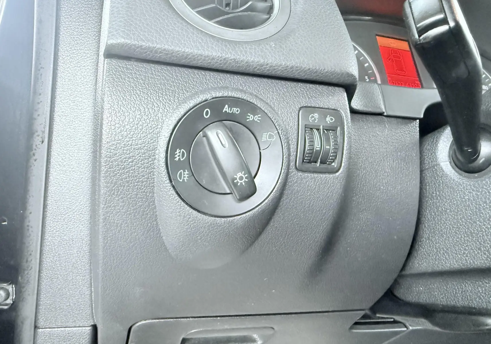Gros plan sur le tableau de bord noir du Volkswagen Tiguan 2007, montrant la molette des phares et les réglages d’éclairage.