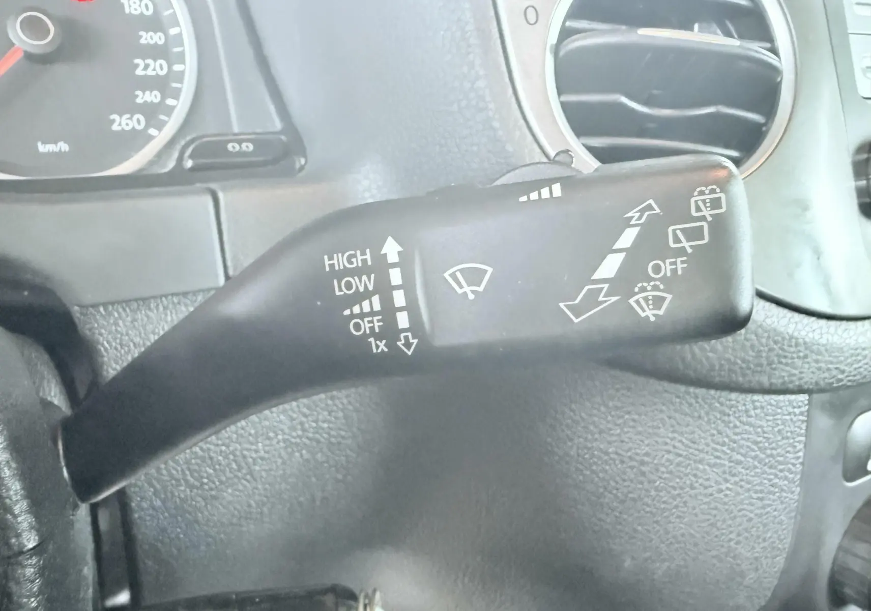 Gros plan sur le commodo noir des essuie-glaces côté gauche du tableau de bord d’un Volkswagen Tiguan noir de 2007.