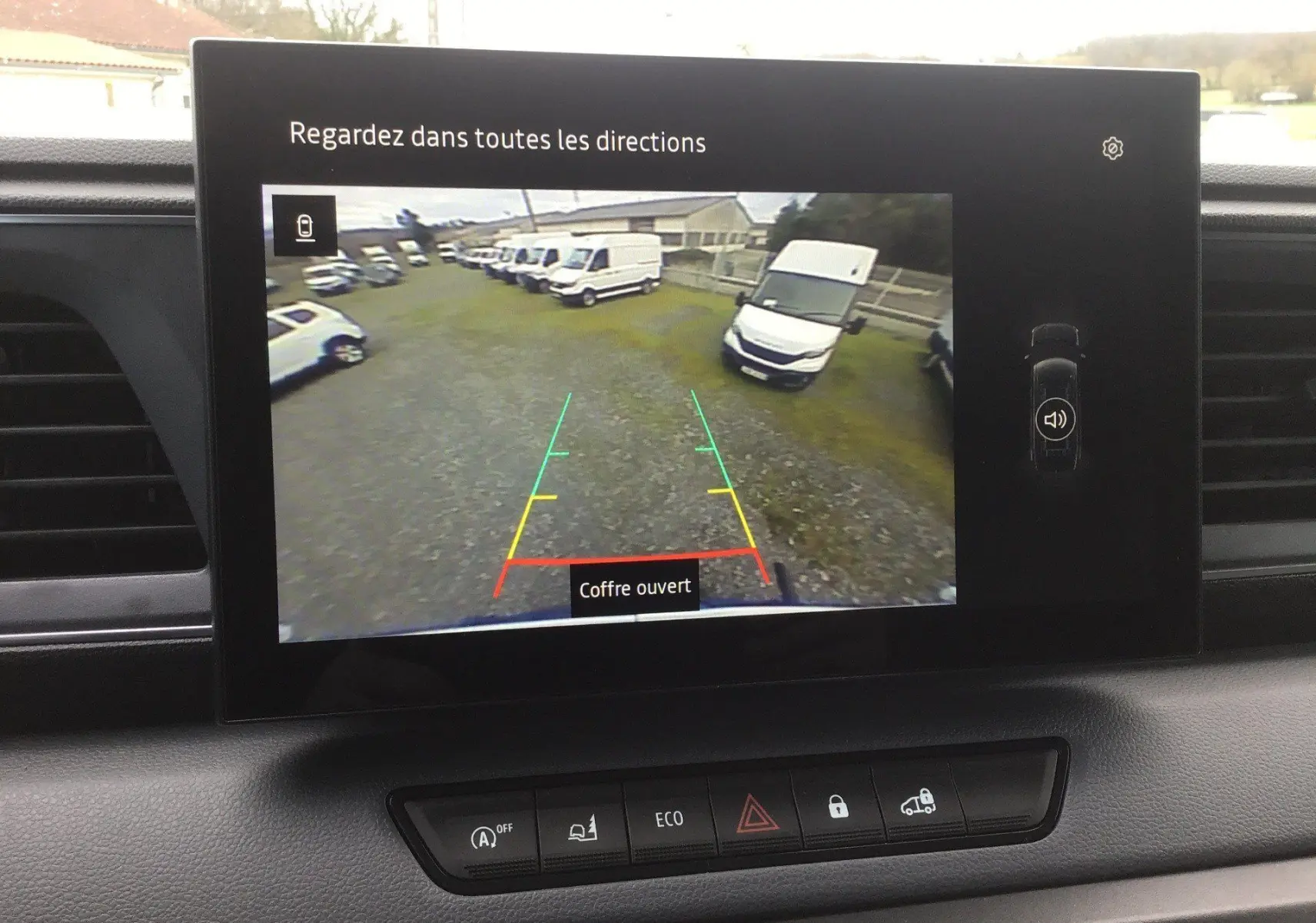 Vue de l'écran de caméra de recul du Renault Master blanc, montrant plusieurs véhicules stationnés sur un terrain gravillonné.