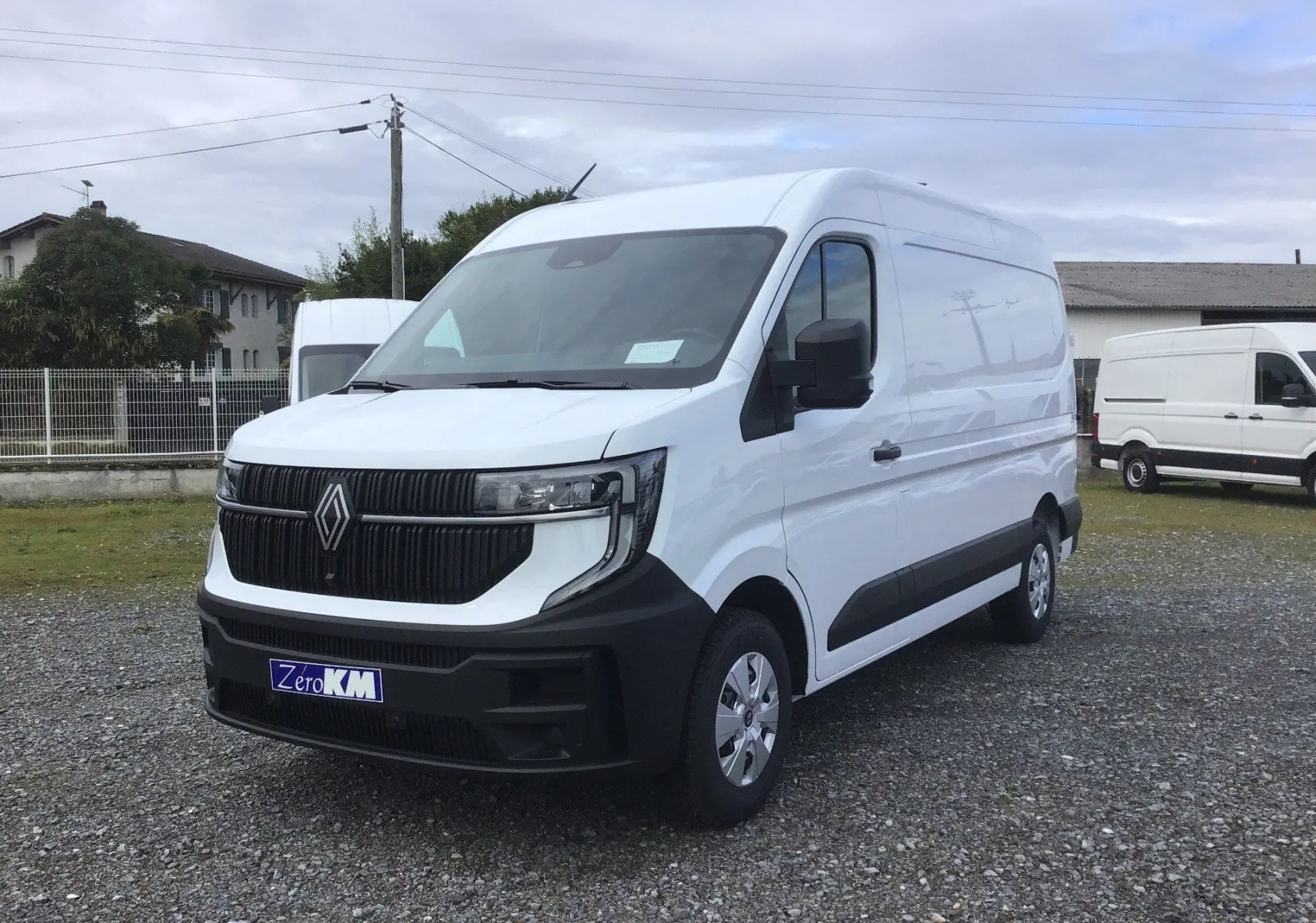 Renault Master blanc en vue 3/4 avant droit, avec calandre noire et pare-chocs noir mat sur terrain gravillonné.
