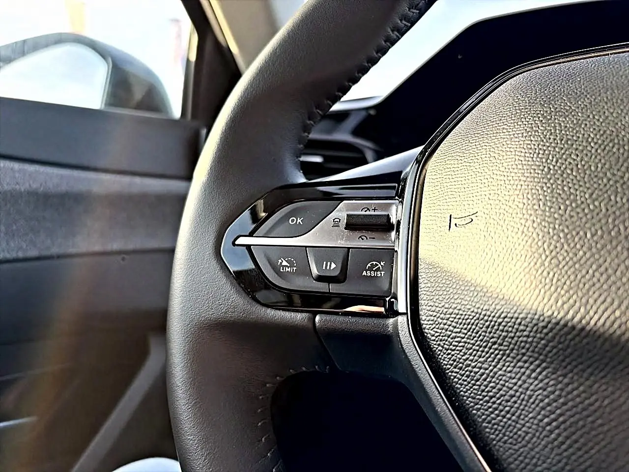 Gros plan sur le volant cuir noir de la Peugeot 408 Hybrid 145 allure, montrant les commandes multifonctions côté gauche.