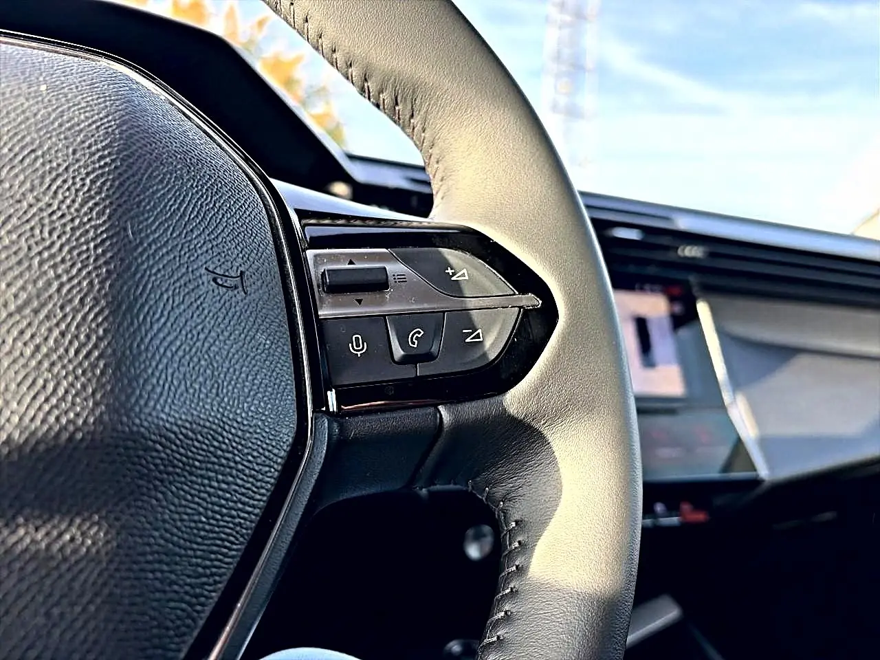Gros plan sur le volant cuir noir de la Peugeot 408 Hybrid 145 allure e-dcs6 avec commandes vocales et téléphone intégrées.