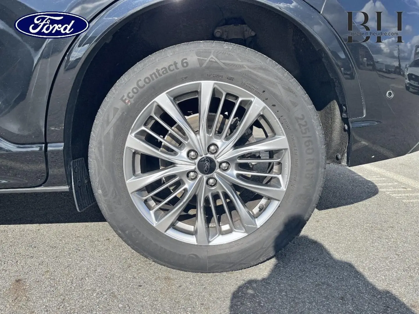 Gros plan sur la roue avant droite du Ford Kuga noir Agate Métallisée avec jante alu multi-branches et logo Ford central.