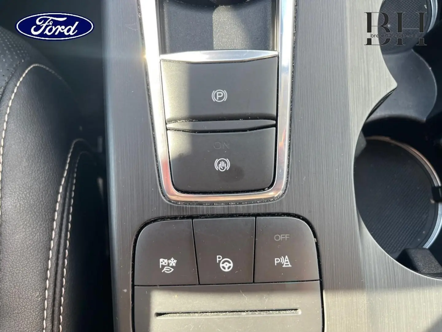 Gros plan sur la console centrale du Ford Kuga noir Agate, montrant les boutons du frein à main électronique et du pack assistance.