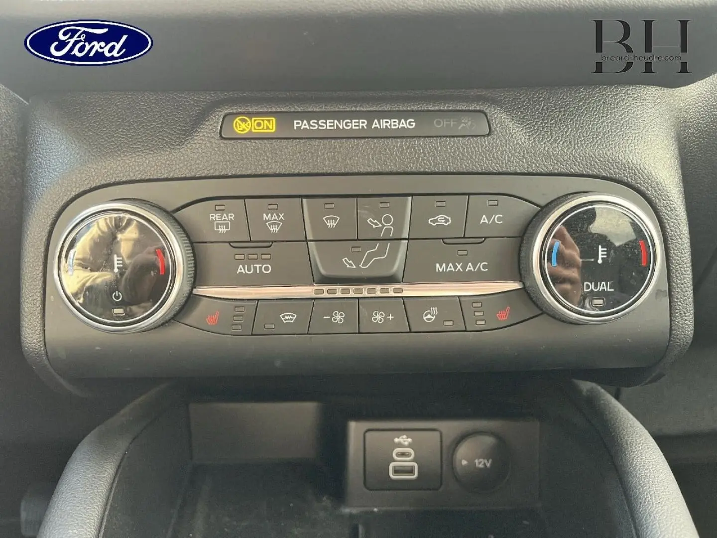 Vue rapprochée de la console centrale du Ford Kuga 2023, avec commandes climatisation bi-zone et ports USB et 12V.