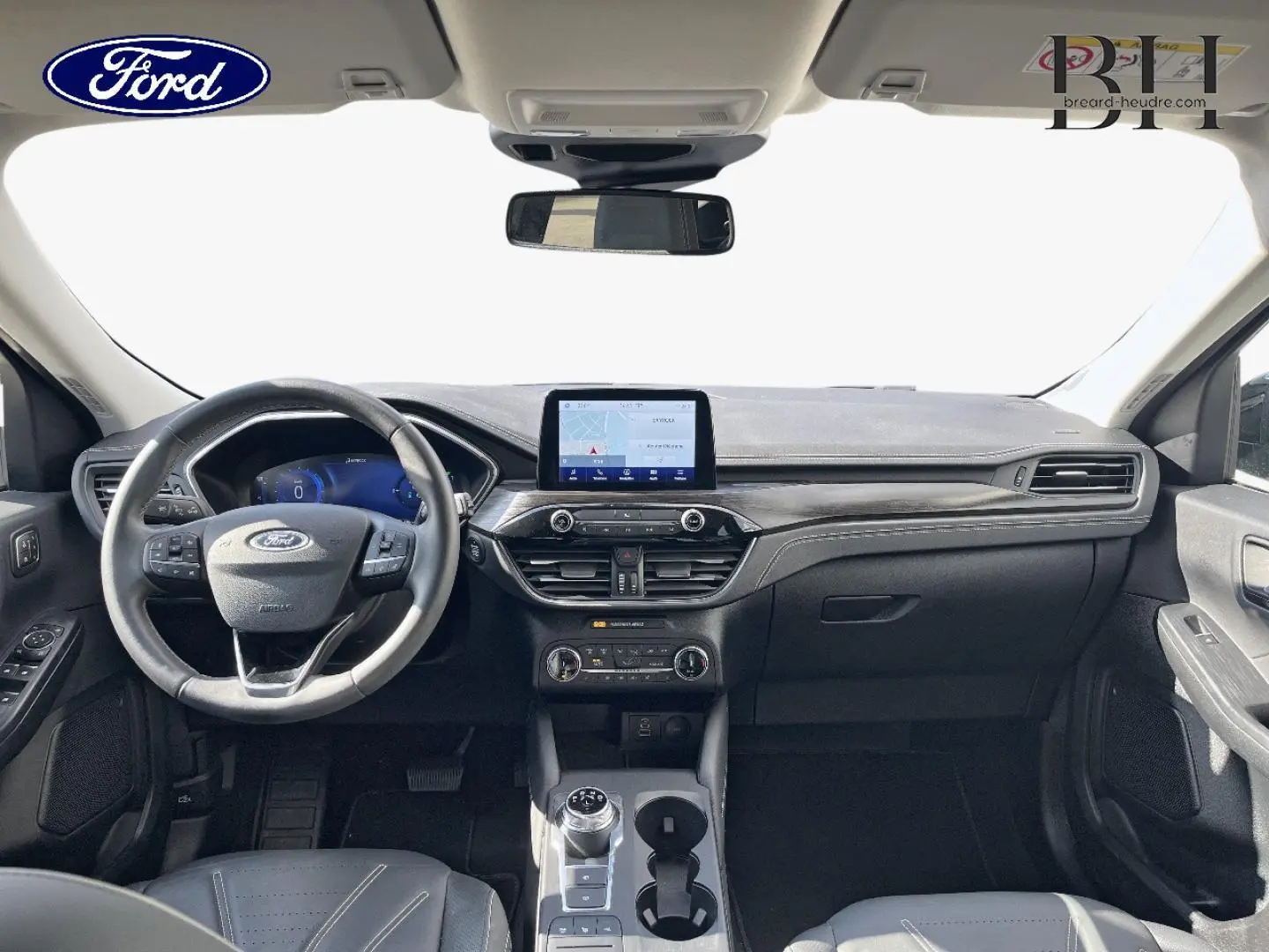 Vue intérieure avant du Ford Kuga 2023, tableau de bord noir avec écran tactile central et volant cuir multifonction.