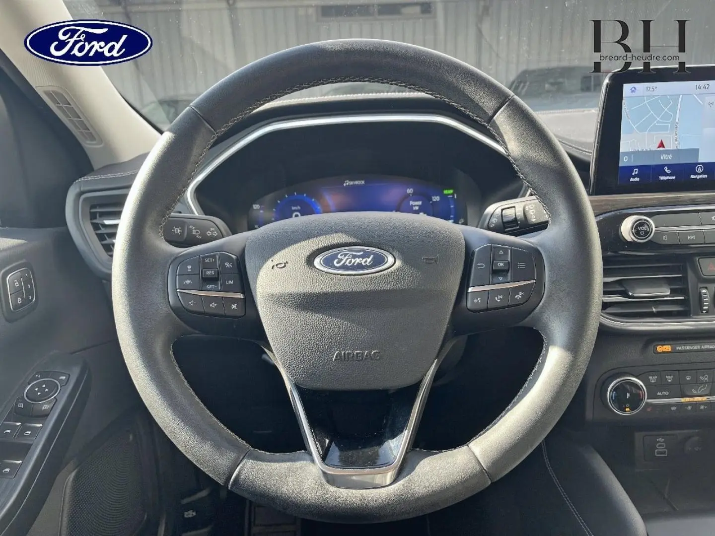 Vue intérieure centrée sur le volant cuir noir du Ford Kuga 2023 avec tableau de bord digital et écran tactile GPS.