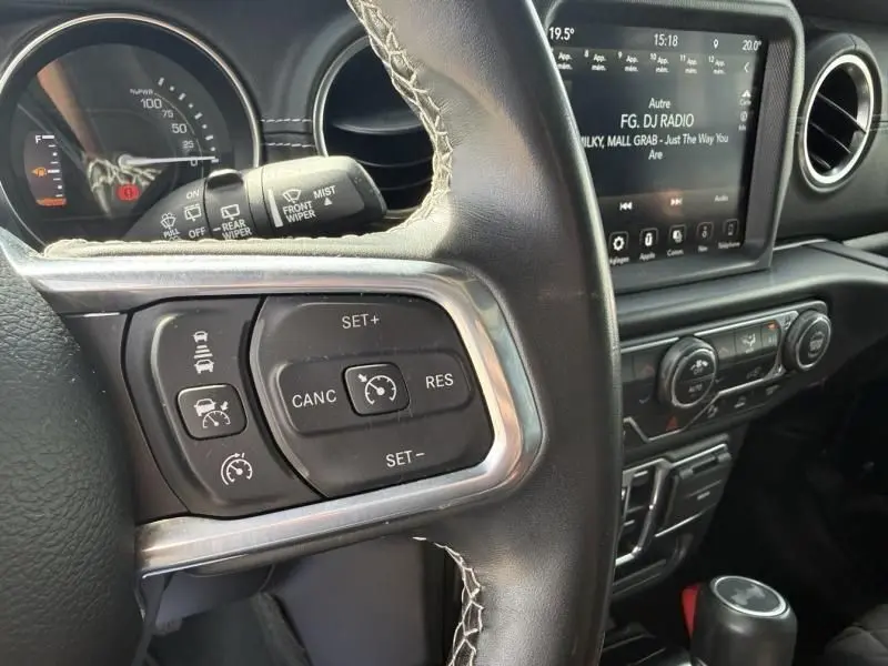 Gros plan sur le volant noir du Jeep Wrangler Unlimited 2022 avec commandes de régulateur et tableau de bord numérique.