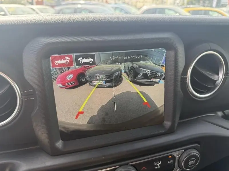 Écran de caméra de recul dans un Jeep Wrangler noir 2022, vue intérieure montrant l'arrière du véhicule et les lignes de guidage jaunes.