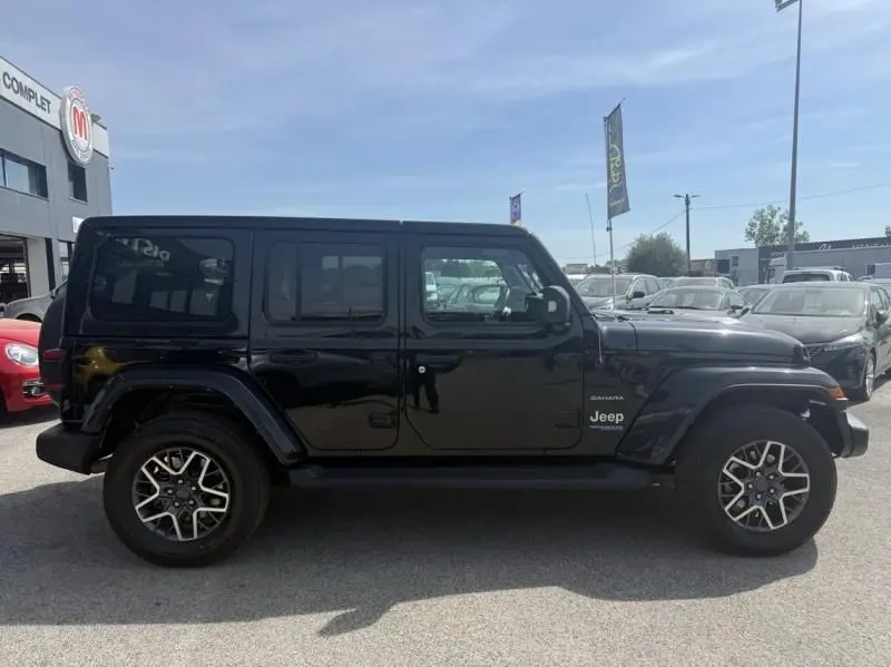 Profil côté gauche d'un Jeep Wrangler Unlimited Sahara noir 2022, hybride rechargeable, avec jantes alliage distinctives.
