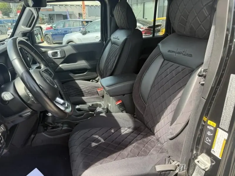 Vue intérieure côté conducteur du Jeep Wrangler Unlimited 2022 noir, sièges avant en tissu matelassé avec logo Sahara brodé.