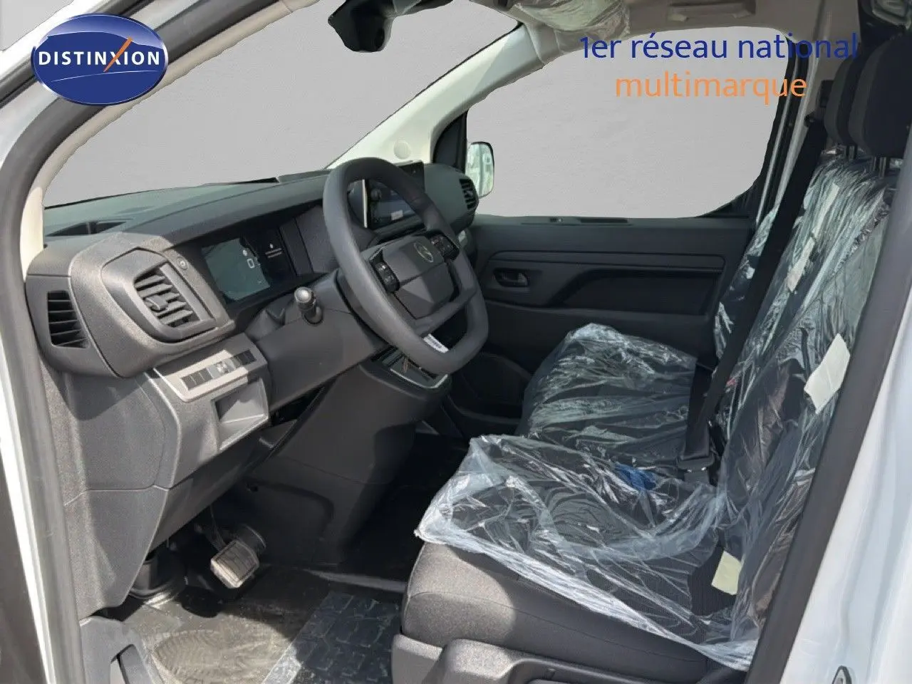 Vue intérieure côté conducteur du Citroën Jumpy blanc Kaolin, sièges protégés par film plastique et tableau de bord moderne.
