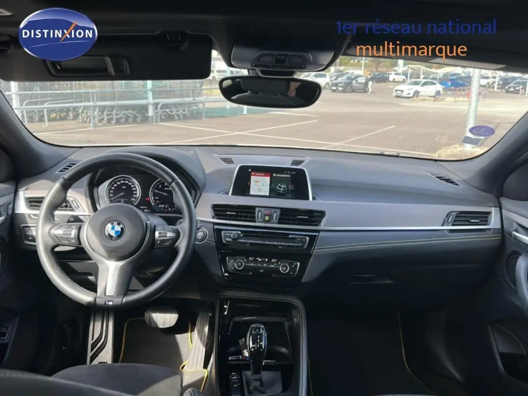 Vue intérieure avant du BMW X2 blanc 2018, volant sport, écran GPS central et tableau de bord moderne.
