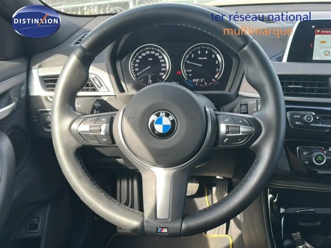 Vue centrée sur le volant sport BMW d’un X2 blanc 2018 avec tableau de bord et écran GPS visibles.