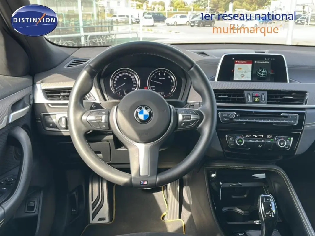 Vue intérieure centrée sur le volant sport et tableau de bord du BMW X2 blanc avec écran GPS et console noire brillante.