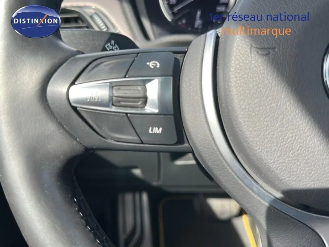 Gros plan sur le volant sport noir de la BMW X2 blanc, montrant les commandes de régulateur de vitesse côté gauche.