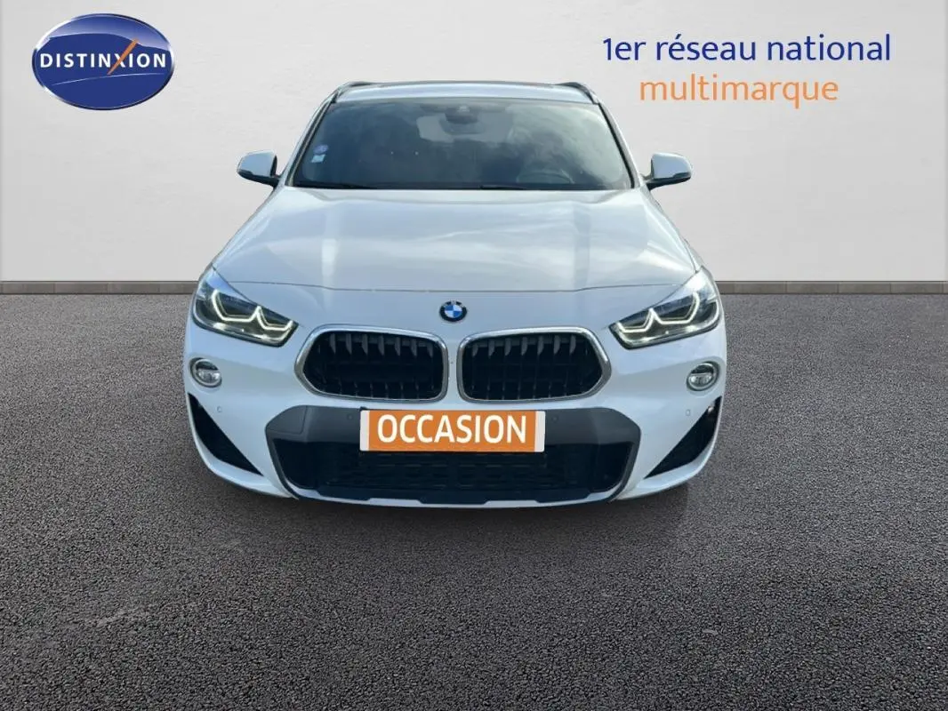 Vue avant d'un BMW X2 blanc avec calandre noire et phares LED allumés sur fond neutre.