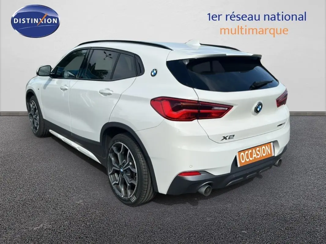 BMW X2 blanc vue 3/4 arrière droit, jantes alliage 19 pouces et toit ouvrant panoramique visibles.