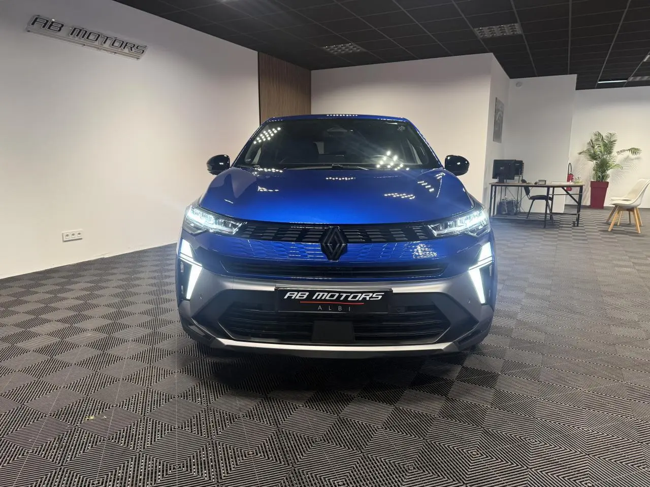 Vue avant d'une Renault Symbioz bleu Iron avec éclairage LED et calandre noire dans un showroom.