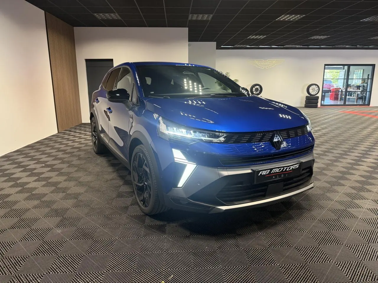 Renault Symbioz bleu Iron en 3/4 avant droit, avec calandre noire et feux LED allumés dans un showroom.