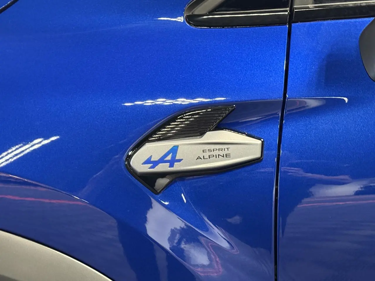 Gros plan sur l'aile avant gauche bleu Iron du Renault Symbioz avec badge Esprit Alpine bleu et noir brillant.