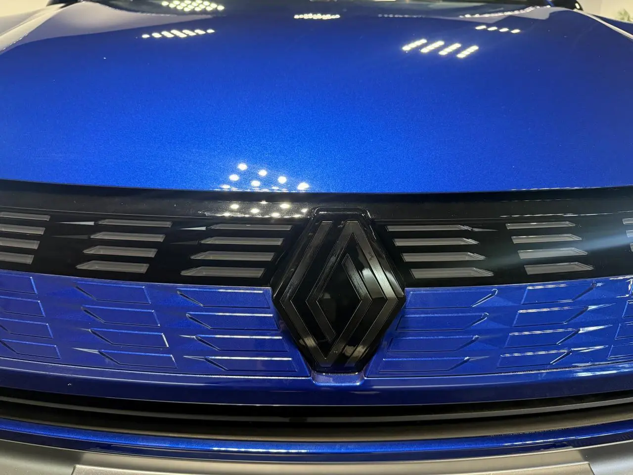 Gros plan sur la calandre avant bleu métallisé du Renault Symbioz avec logo noir brillant au centre.