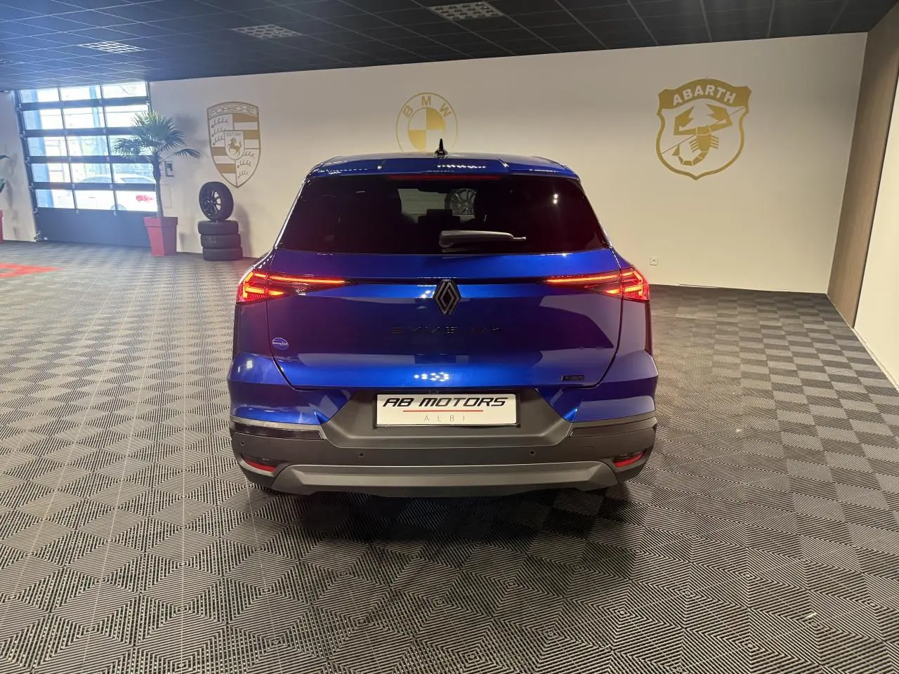 Vue arrière d'un Renault Symbioz bleu Iron 2025 avec feux LED allumés et logo Alpine dans un showroom.