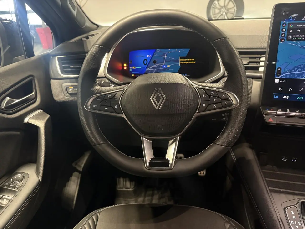Vue intérieure centrée sur le volant noir de la Renault SYMBIOZ 2025 avec tableau de bord numérique et écran tactile latéral.