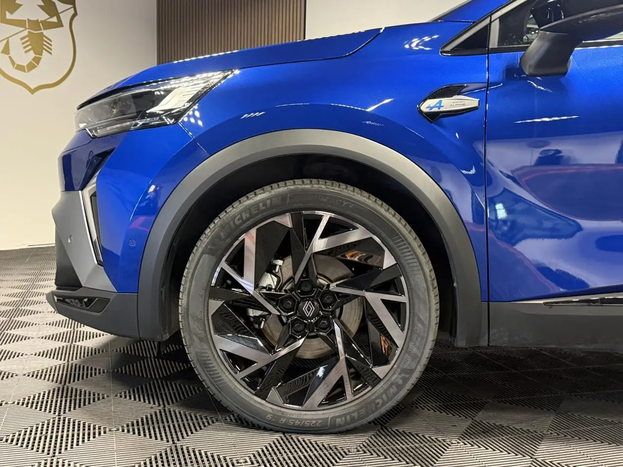Gros plan sur la roue avant gauche et l’aile d’une Renault SYMBIOZ bleu Iron avec badge Esprit Alpine visible.