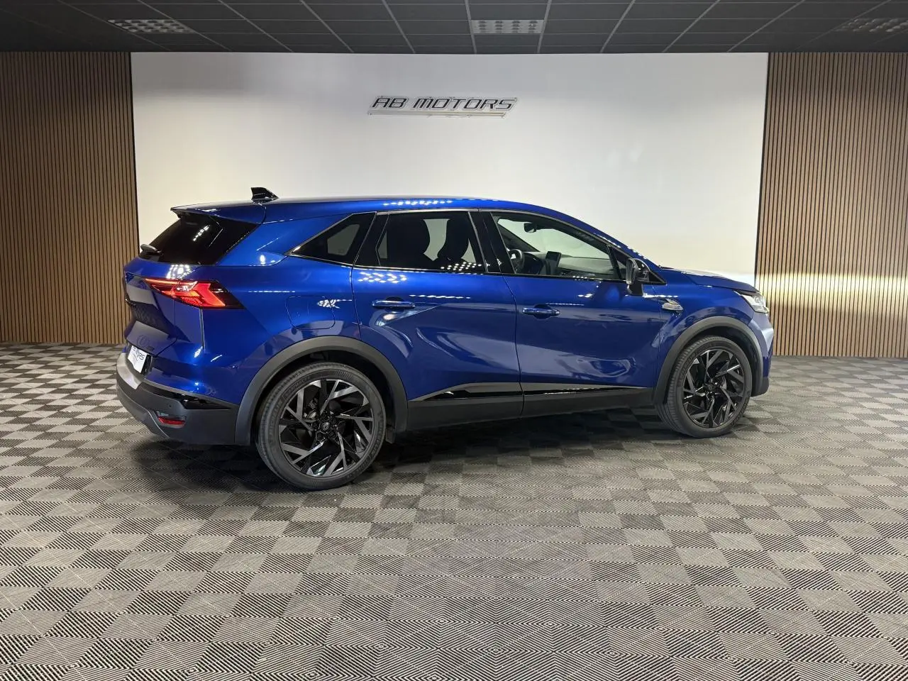 Vue latérale droite du Renault Symbioz 1.6 E-Tech Hybride bleu Iron avec jantes noires et détails noirs brillants.