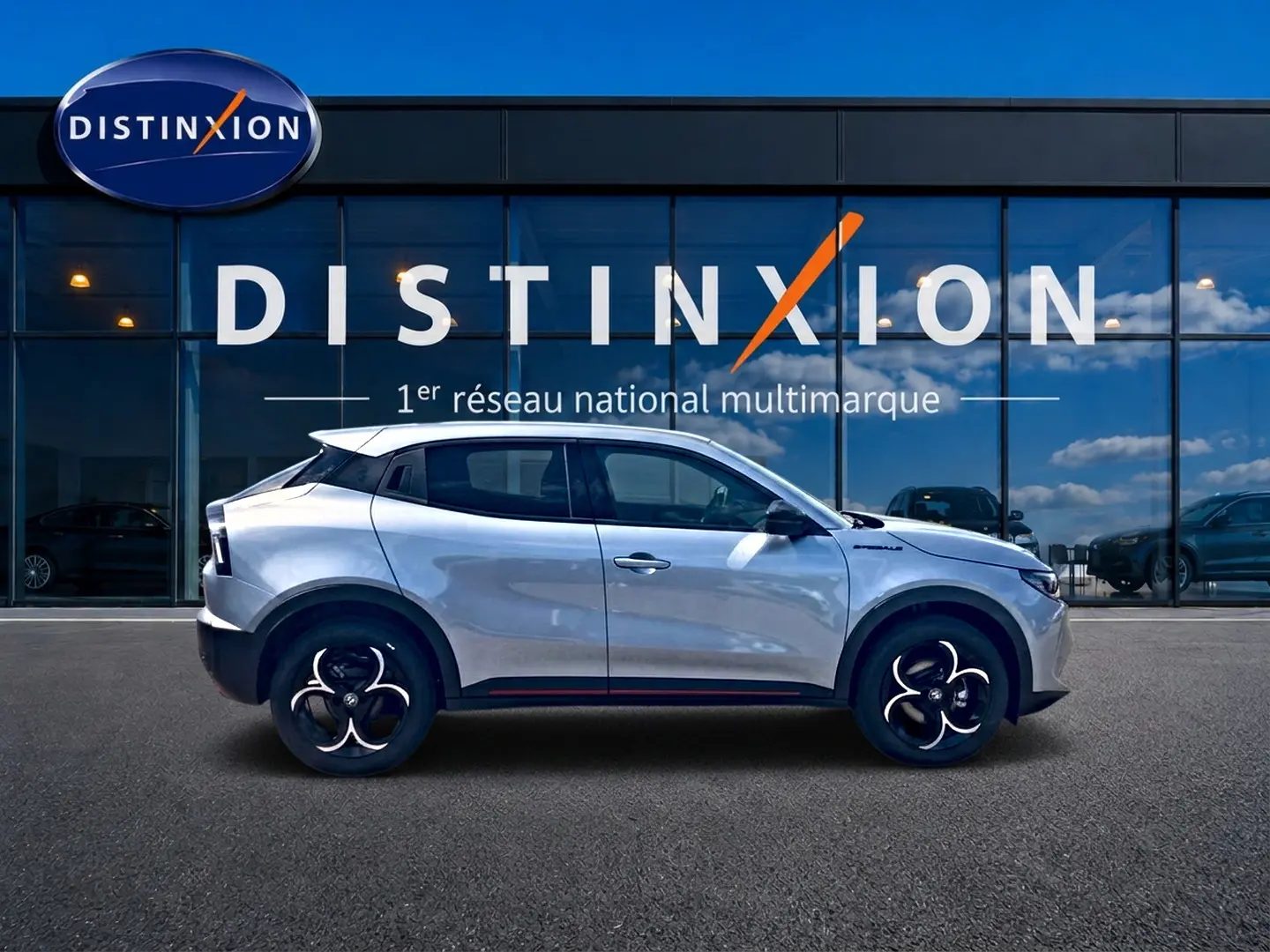 Vue de profil droit de l'Alfa Romeo Junior 1.2 hybride gris avec jantes en alliage devant une vitrine Distinxion.