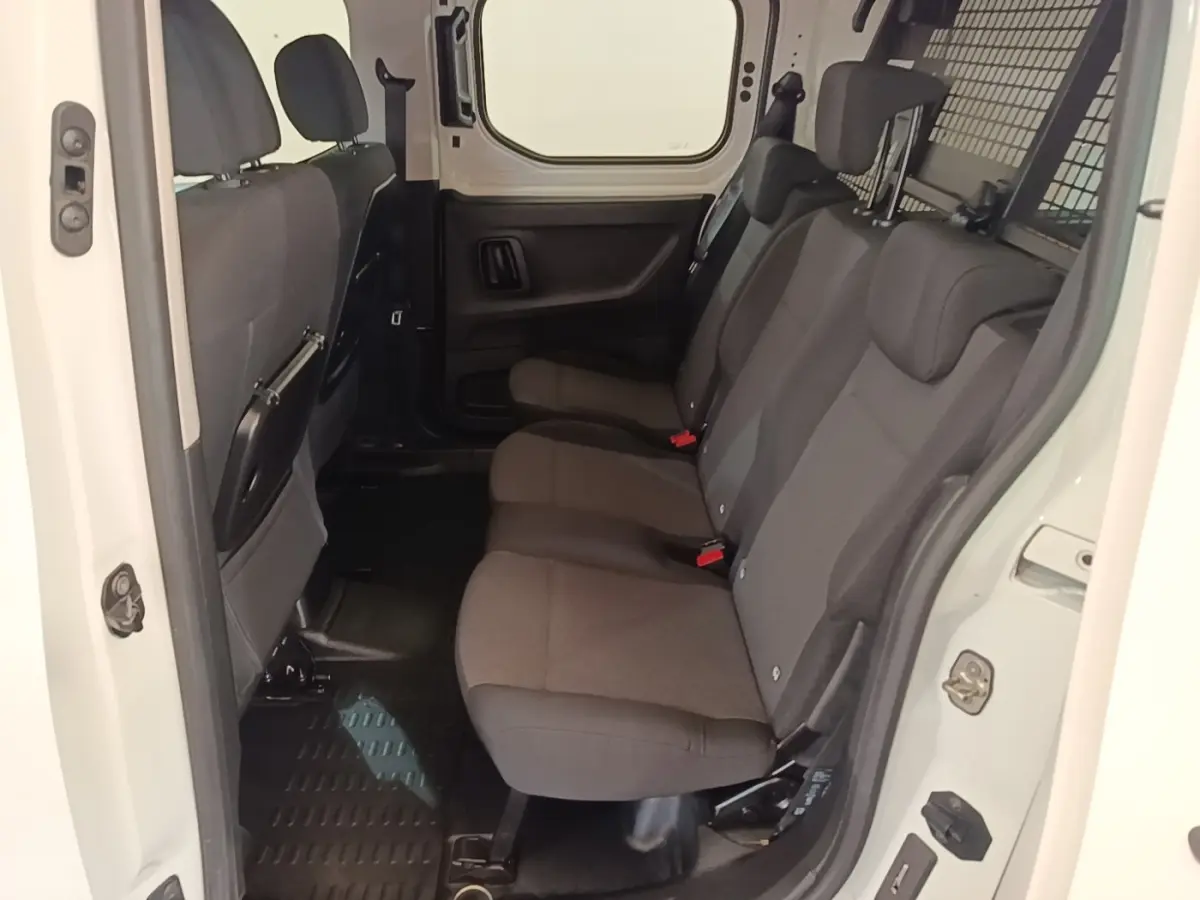 Vue intérieure côté droit sur la banquette arrière grise du Peugeot Partner blanc avec cloison grillagée pleine.