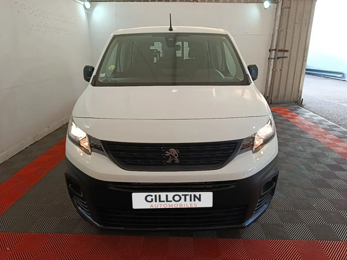 Vue avant d'un Peugeot Partner blanc avec calandre noire et pare-chocs noir dans un garage fermé.