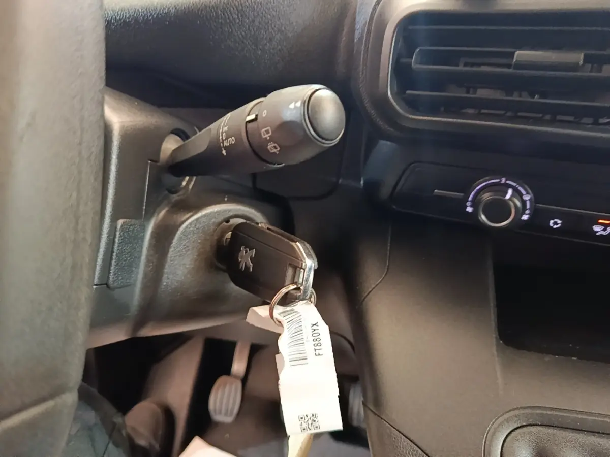 Gros plan intérieur sur le contacteur avec clé Peugeot insérée, volant et commandes noires visibles en arrière-plan.